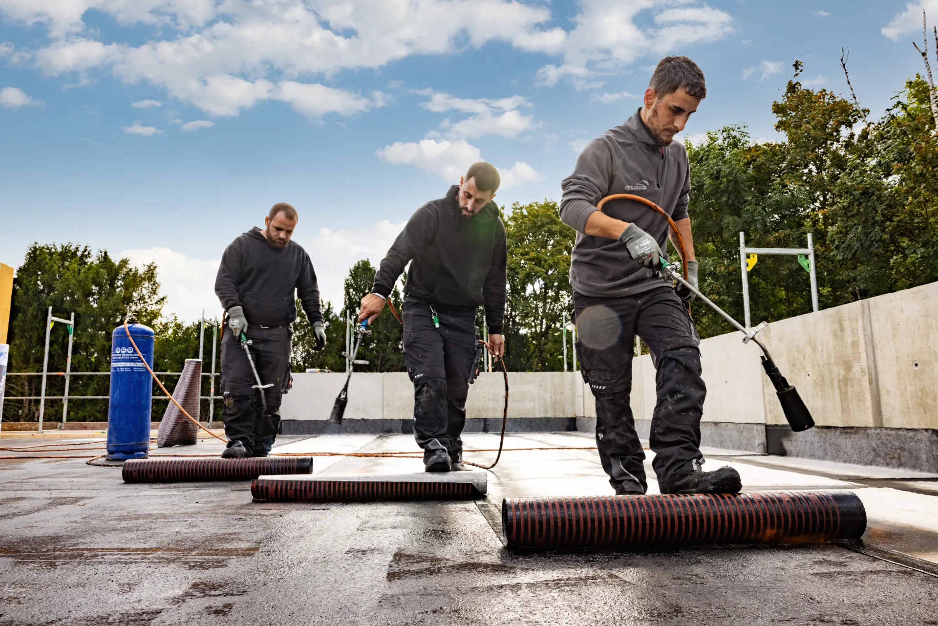 Arbeiter verlegen Bitumenbahnen auf einem Flachdach.