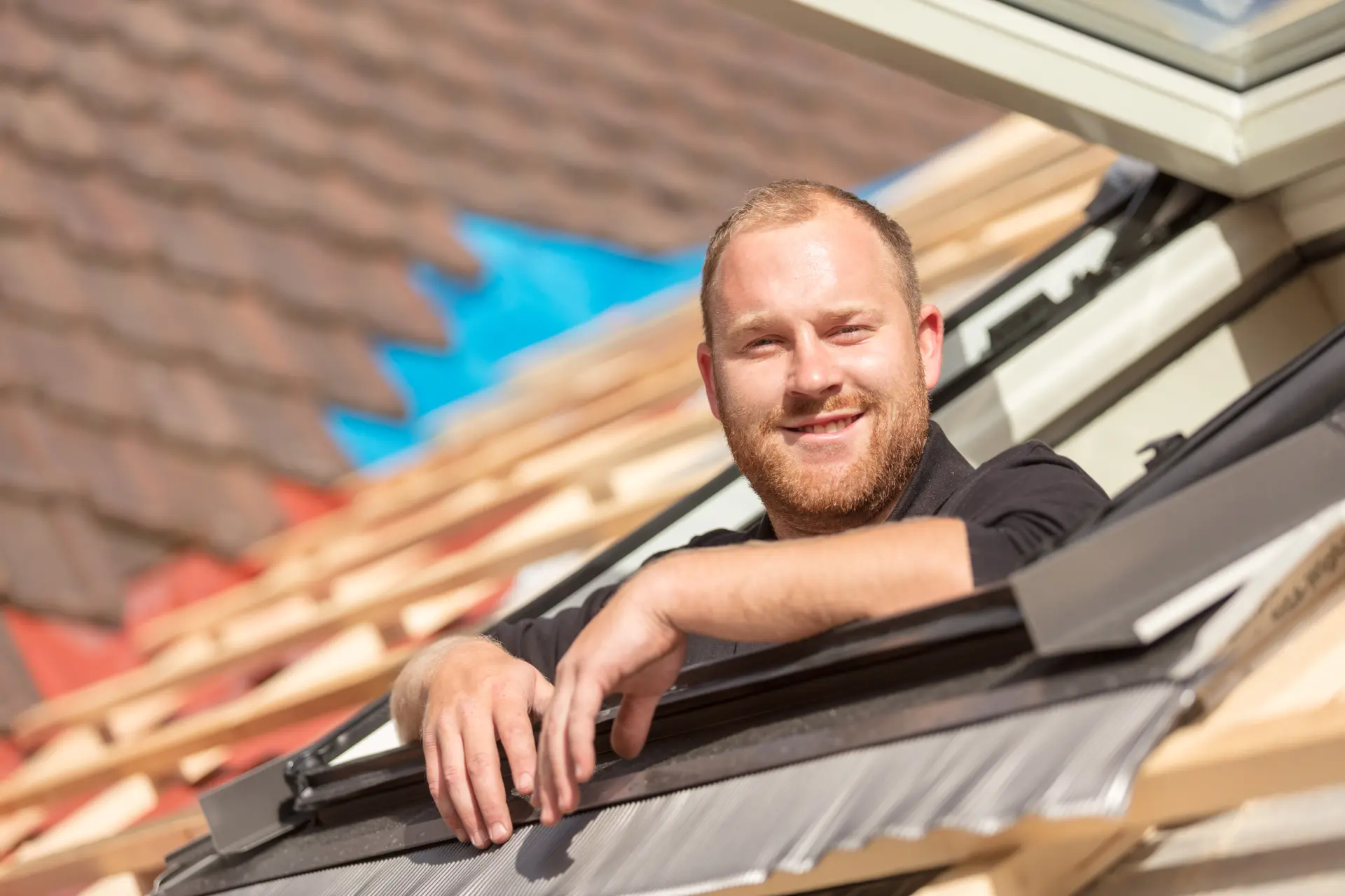 Ein Mann lehnt freundlich aus einem neu eingebauten Dachfenster.