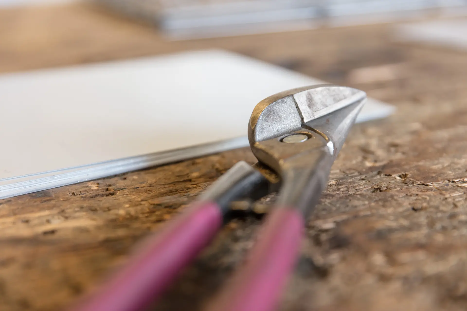 Eine Blechschere liegt auf einer Werkbank, im Hintergrund befinden sich Metallplatten.