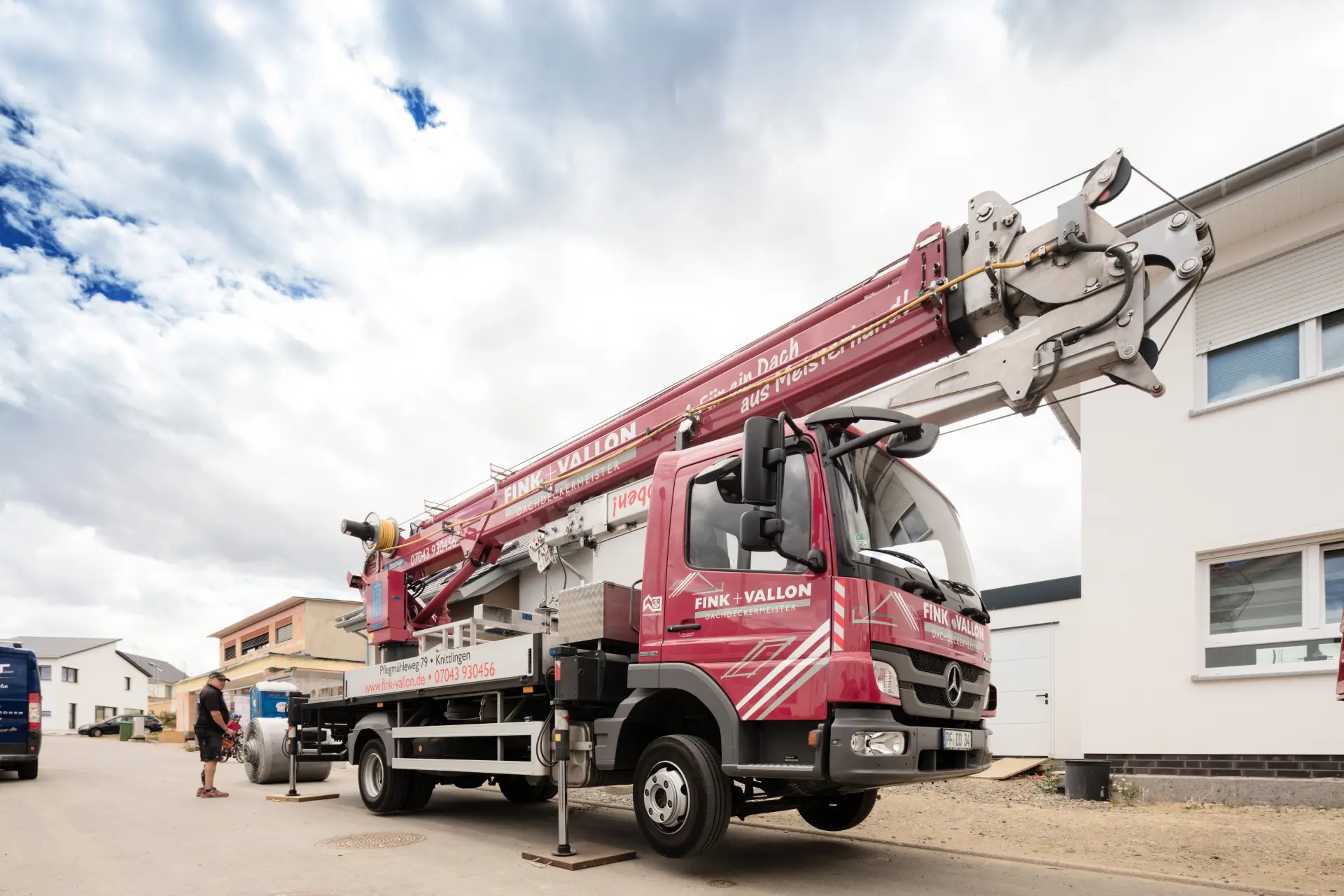 Ein großer roter Kranwagen mit der Aufschrift „Fink + Vallon“ steht vor einem Haus.