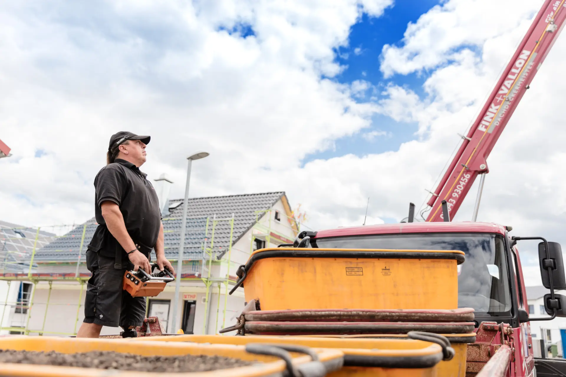 Ein Mann steuert mit einer Fernbedienung den Baukran, vor ihm stehen mehrere große gelbe Behälter.